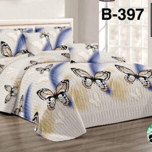 A well-lit bedroom showcases a Queen-King 5 Piece Quilt Set. The bed is adorned with a quilt and pillowcases decorated with large black and white butterflies on a gradient blue and beige background. The B-397 set includes 1x quilt, 2x continental pillowcases, and 2x standard pillowcases.