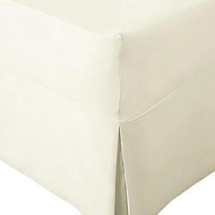Close-up of a corner section of a cream bed skirt with a tailored design. Part of a combo set, the bed skirt features a neat pleat at the corner, draping smoothly to the floor. The fabric appears soft and pastel in color.