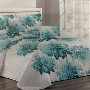A bed with a floral turquoise and white quilt and matching pillows, set against a bright, airy room with natural light.
