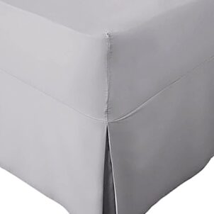 Close-up of a corner section of a light grey bed skirt with a tailored design. Part of a combo set, the bed skirt features a neat pleat at the corner, draping smoothly to the floor. The fabric appears soft and pastel in color.