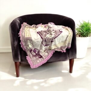 A 150cm x 150cm Charlie fringe blanket in a calming purple color, featuring a cozy, warm pattern and soft fringe detailing along the edges. Weighing 500g, this lightweight yet comfortable blanket is perfect for adding warmth and texture to any sofa, bed, or reading nook.